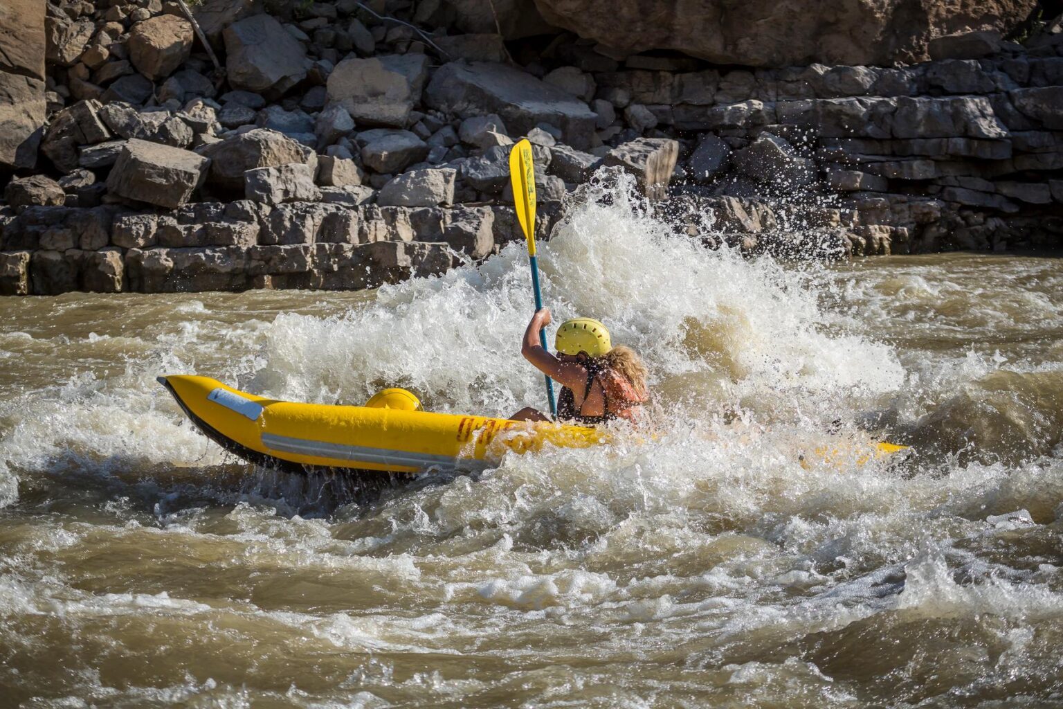 A person paddles an inflatable kayak through a splash rapid along the Green River in Desolation Canyon.