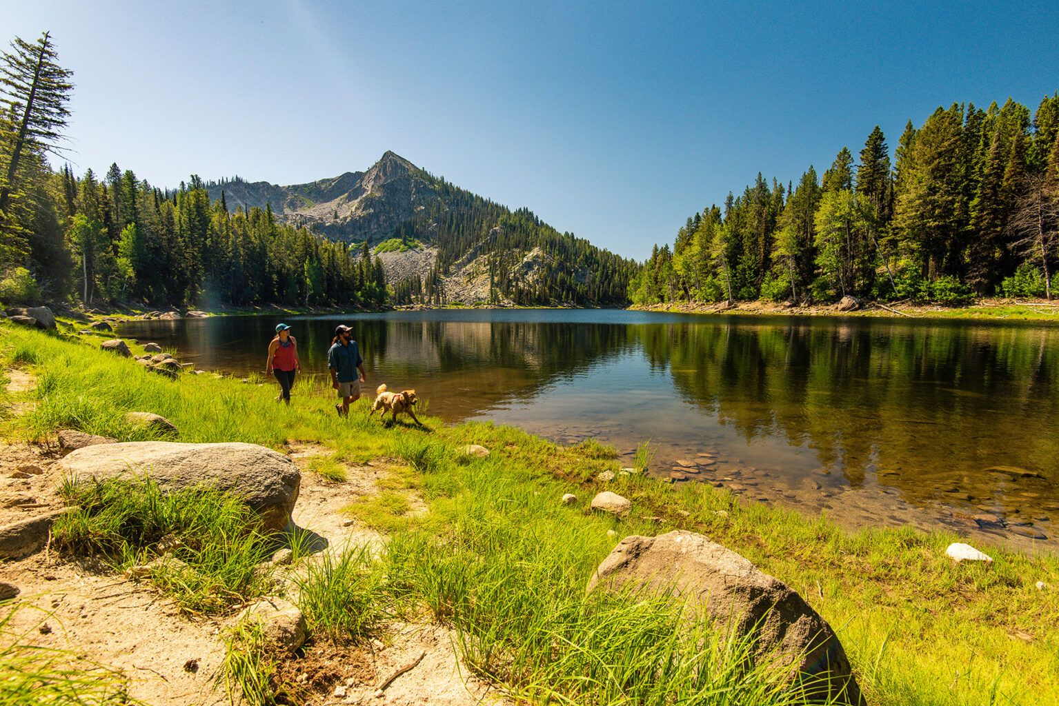 A couple walks along a trail next to scenic mountain lake