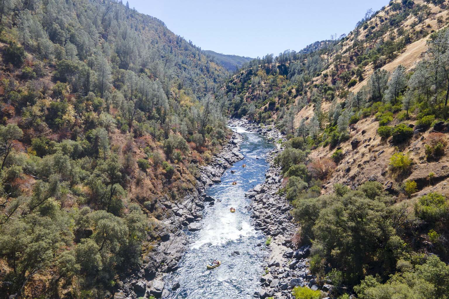 Upstream canyon view of the Wild & Scenic Tuolumne River with tiny yellow rafts dotting the river