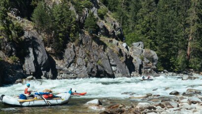 A white raft and kayakers hitting whtiewater on the Selway River